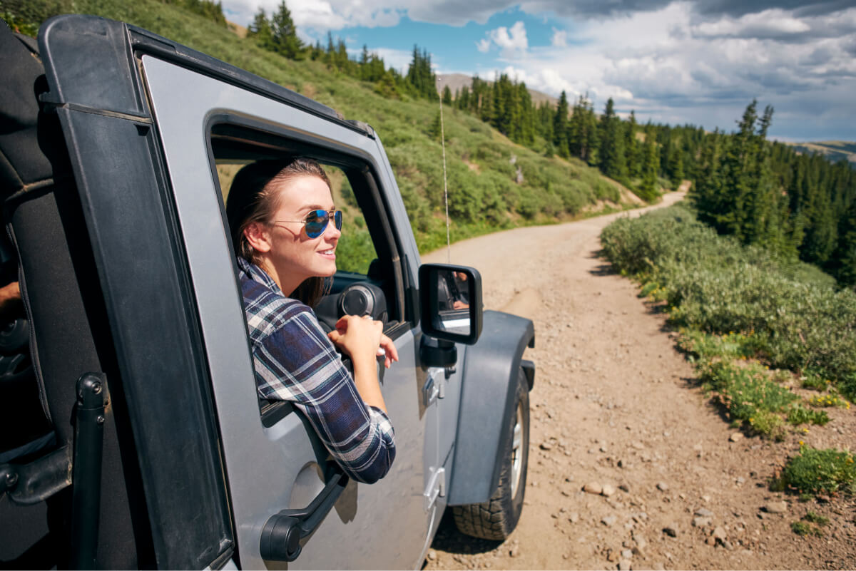 Colorado woman in sunglasses enjoying the blue sky weather and being driven on a mountainous Colorado dirt road
