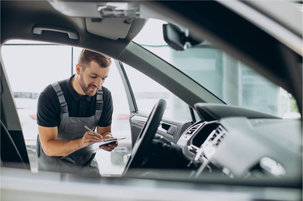 Male auto mechanic inspecting interior of a vehicle with clipboard in hand