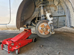 car without wheel raised by floor jack to expose brake rotor and caliper