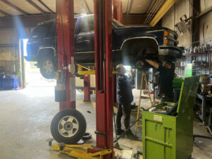 two mechanics at Leo's Auto Body in Littleton performing a auto maintenance and repair services on a lifted SUV